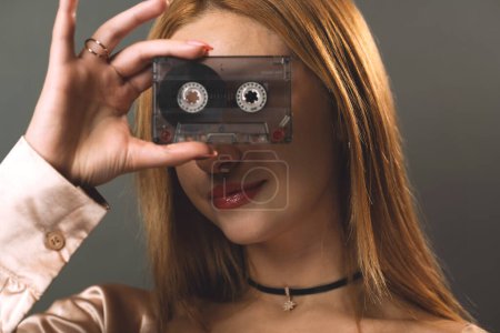 Foto de Una mujer joven oscurece creativamente sus ojos con una cinta de cassette de música vintage. - Imagen libre de derechos