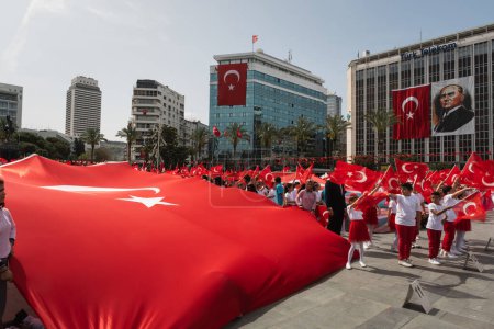 Téléchargez les photos : Izmir, Turquie - 23 avril 2024 : Au cours de la Journée nationale de la souveraineté et de l'enfance, les enfants étendent un énorme drapeau turc sur la place de la République d'Izmir, avec plus de participants courant vers l'avant, un drapeau géant et un portrait d'Atatürk visible derrière. - en image libre de droit