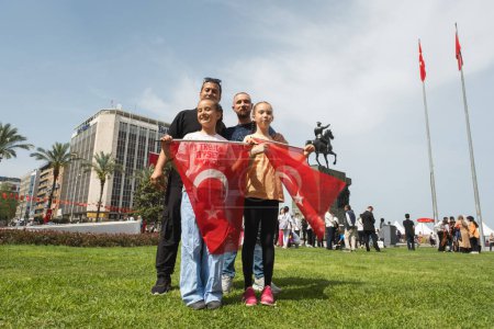 Photo for Izmir, Turkey - April 23, 2024: Amidst Children's Day celebrations at Republic Square, two girls with flags stand proudly with their father, with the majestic equestrian statue in the background - Royalty Free Image