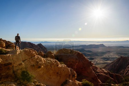 A male hiker stands confidently on a mountain summit overlooking the stunning view of the Las Vegas skyline - Red Rock National Conservation Area, Nevada, USA