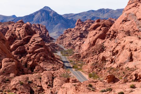 Stunning view of the iconic Mouses Tank Road running through an epic red sandstone canyon with otherworldly boulders. Mountains frame the background - Valley of Fire State Park, Nevada, USA