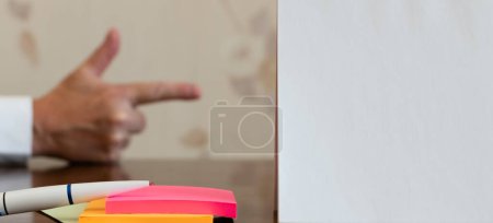 White sheet of paper and ballpoint pen on multi-colored paper stickers close-up on blurred background of forefinger of middle-aged man