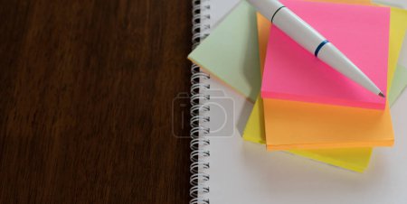 Multicolored paper stickers, white ballpoint pen and white sheet of diary close-up on wooden table. Top view