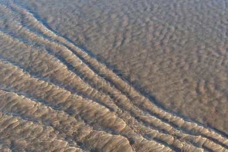 Verschwommenes Bild von feinem, zartem Küstensand am Strand unter einer dünnen Schicht transparenten Meerwassers