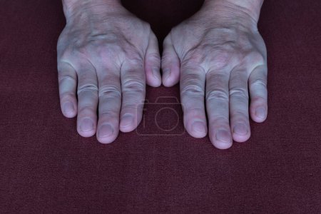 Hands wrists of an elderly man close-up on dark cloth background