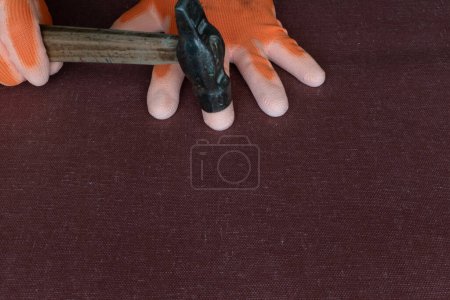 Frappe de marteau métallique sur le doigt dans un gant de protection sur le lieu de travail