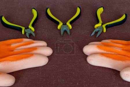 Set Zangen-Werkzeuge und orangefarbene Isolierhandschuhe auf dunklem Stoff-Hintergrund