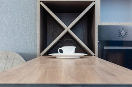 Kitchen cabinet furniture. White cup and plate on wooden table close-up against background of kitchen furniture