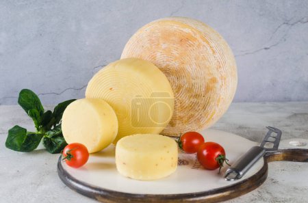 Foto de Una pila de diferentes tipos de cabezas de queso apiladas en la mesa. Cabezas de queso duro medio sobre tabla de cortar de madera. Concepto de alimentación orgánica saludable. Queso hecho a mano. - Imagen libre de derechos