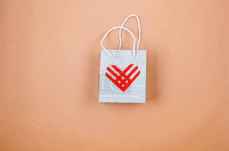 Photo for Red linear paper hearts over grey bag on light beige background. Giving Tuesday, the global day of charity. give help, donations support concept. - Royalty Free Image
