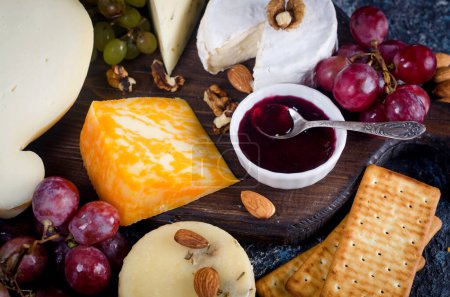Assorted homemade pieces cheese with jam, grapes, cookies and nuts, cookies and nuts on table.  Fresh dairy product, cheese snack, healthy organic food. Delicious appetizer.