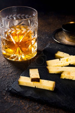 Pieces hard "dry jack" cheese in a coffee crust and a glass of whiskey. gourmet snack.