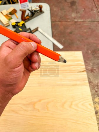 Téléchargez les photos : Main tenant un crayon orange entre ses doigts et en arrière-plan une partie de sa table et de son outil de travail - en image libre de droit