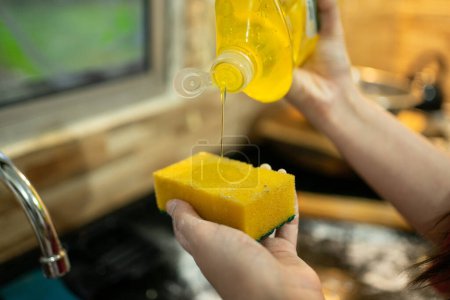 Foto de Verter jabón líquido en una esponja para limpiar los utensilios de cocina utilizados para los bollos de queso - Imagen libre de derechos