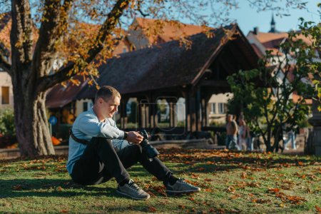 Foto de Fotógrafo profesional tomando fotos de hermoso parque de otoño. hombre fotógrafo profesional sentarse con la cámara en el parque de otoño - Imagen libre de derechos