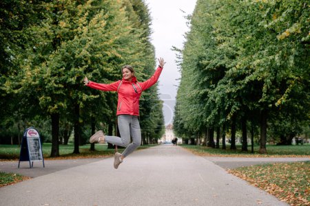 Téléchargez les photos : Jeune femme caucasienne fille avec dents sourire sauter dans la forêt du parc en plein air en regardant la caméra. - en image libre de droit