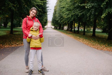 Foto de Madre e hijo de pie abrazándose en el parque en el otoño. feliz madre jugando con su hijo en el parque. Madre abraza a su hijo mientras está de pie en el bosque en otoño. - Imagen libre de derechos