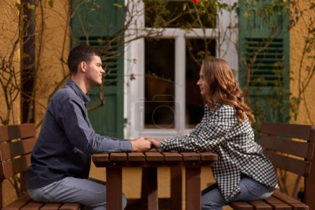 Happy smiling young dating couple having coffee together and enjoying life sitting at table holding hands in street cafe on summer day. Pretty man and woman spending time together enjoying weekend
