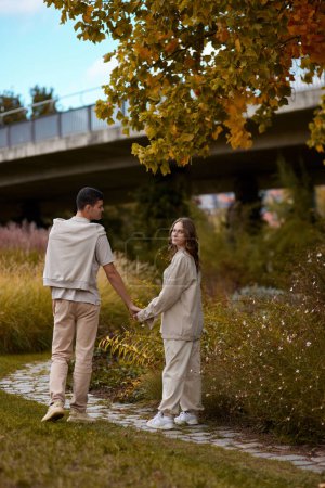 Young couple in love walking in the autumn park holding hands looking in the sunset. Closeup of loving couple holding hands while walking at sunset. The hands of the male and female lovers who hold