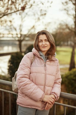 Young beautiful pretty tourist girl in warm hat and coat with backpack walking at cold autumn in Europe city enjoying her travel in Zurich Switzerland. Outdoor portrait of young tourist woman enjoying