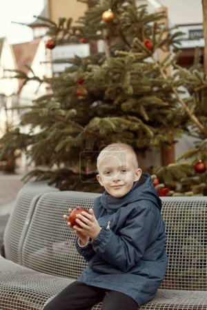 Winter Wonderland Delight: 8-jähriger Junge mit Weihnachtsdekor am Vintage Fountain. Erleben Sie die Magie der Winterfreude mit diesem bezaubernden Bild, in dem ein wunderschöner 8-jähriger Junge auf einem