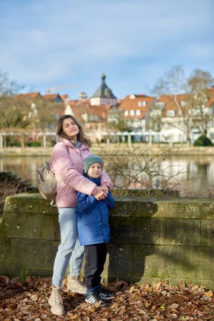 Riverside Family Harmony: Mother, 30 Years Old, and Son - Beautiful 8-Year-Old Boy, Standing by Neckar River and Historic Half-Timbered Town, Bietigheim-Bissingen, Germany, Autumn. Immerse yourself in