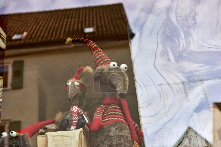 Whimsical New Years Mouse in Cap and Scarf Stands Behind Store Display. Capture the charm of the holiday season with this delightful image featuring a toy mouse or rat wearing a comical New Years