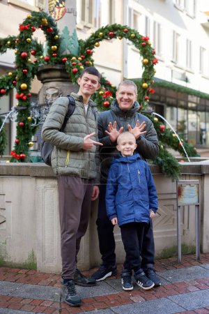Joyful Family Portrait: Father and Two Sons by Festive Vintage Fountain. Capture the essence of familial happiness with this heartwarming image featuring a handsome father with his two sons standing