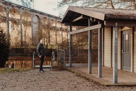 Élégance intemporelle : Homme de 40 ans veste élégante au bord de la rivière Neckar et pont historique à Bietigheim-Bissingen, Allemagne. Découvrez l'attrait des saisons comme un homme charismatique de 40 ans se tient