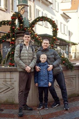 Joyful Family Portrait: Father and Two Sons by Festive Vintage Fountain. Capture the essence of familial happiness with this heartwarming image featuring a handsome father with his two sons standing