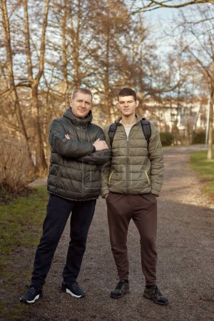 Father-Son Bond: Handsome 40-Year-Old Man and 17-Year-Old Son Standing Together in Winter or Autumn Park. Capture the essence of familial connection with this heartwarming image featuring a handsome