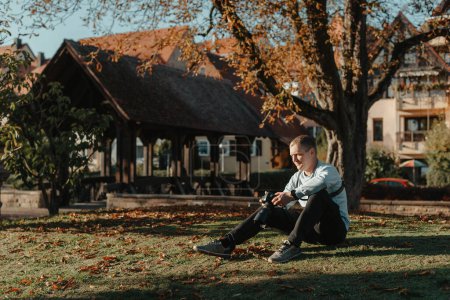 Téléchargez les photos : Photographe professionnel photographiant un magnifique parc d'automne. homme photographe professionnel assis avec appareil photo dans le parc d'automne - en image libre de droit