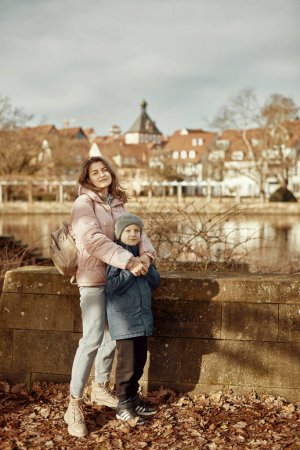 Riverside Family Harmony: Mutter, 30 Jahre alt, und Sohn - Schöner 8-jähriger Junge, am Neckar stehend und historische Fachwerkstadt, Bietigheim-Bissingen, Deutschland, Herbst. Eintauchen in