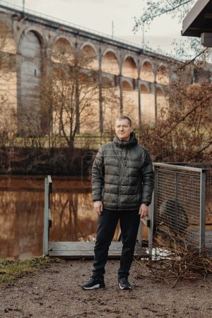 Zeitlose Eleganz: 40-jähriger Mann in schicker Jacke am Neckar und historischer Brücke in Bietigheim-Bissingen. Erleben Sie den Reiz der Jahreszeiten als charismatischer 40-jähriger Mann