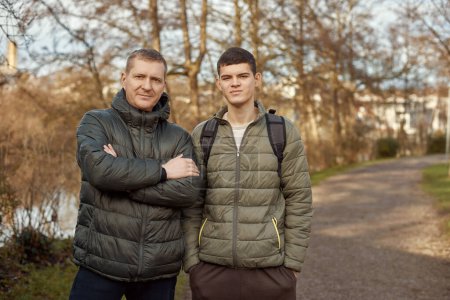 Father-Son Bond: Handsome 40-Year-Old Man and 17-Year-Old Son Standing Together in Winter or Autumn Park. Capture the essence of familial connection with this heartwarming image featuring a handsome