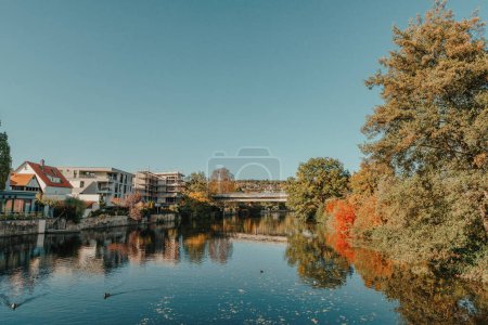Schöne kleine Fluss mit sauberem und klarem Wasser vor bunten Herbstbäumen und kleine Altstadt auf dem Hügel gegen ist schön blau und Wolken Himmel im Herbst in Europa.