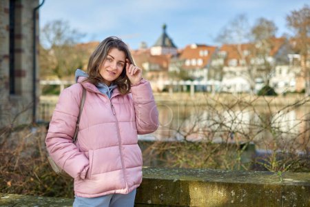 Young beautiful pretty tourist girl in warm hat and coat with backpack walking at cold autumn in Europe city enjoying her travel in Zurich Switzerland. Outdoor portrait of young tourist woman enjoying
