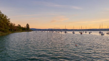 Bodensee Lake Panorama. Tarde, crepúsculo, puesta de sol, pintoresco paisaje, aguas serenas, barcos y yates en el muelle, hermoso cielo con nubes reflejándose en el agua, ribera al atardecer