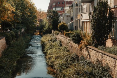 Schöne kleine Fluss mit sauberem und klarem Wasser vor bunten Herbstbäumen und kleine Altstadt auf dem Hügel gegen ist schön blau und Wolken Himmel im Herbst in Europa.