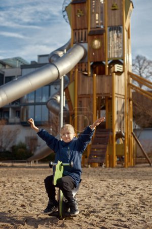 Kinderfreude: Schöner 8-jähriger Junge in Jacke schwingt auf Pferdewippe, Hintergrund des Spielparks in Bietigheim-Bissingen, Deutschland, Herbst. Die reine Essenz des Glücks in der Kindheit einfangen