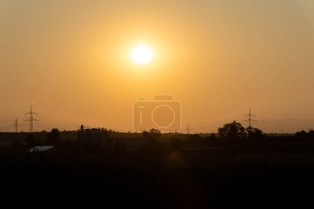 Photo for Sunset above power lines and farm silhouettes with clear sky - Royalty Free Image