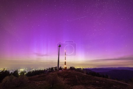 pink colorful northern lights sky above bismarckturm on hornisgride in Baden-wuerttemberg, germany and city lights in background