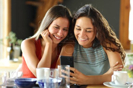 Foto de Vista frontal de dos amigos felices comprobando smart pone en un restaurante - Imagen libre de derechos