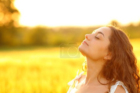 Entspannte Frau atmet bei Sonnenuntergang frische Luft in ländlicher Umgebung