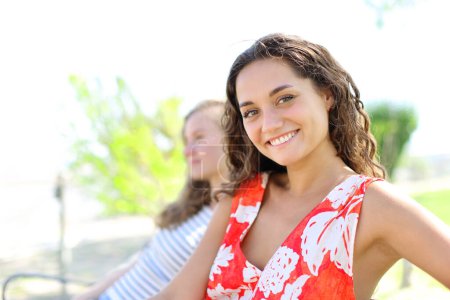 Foto de Mujer feliz con un amigo mirando la cámara sentada en un banco - Imagen libre de derechos