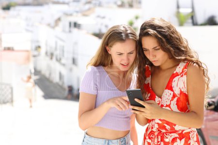 Téléchargez les photos : Deux touristes inquiets vérifier smart phone nouvelles en ligne sur les vacances d'été - en image libre de droit