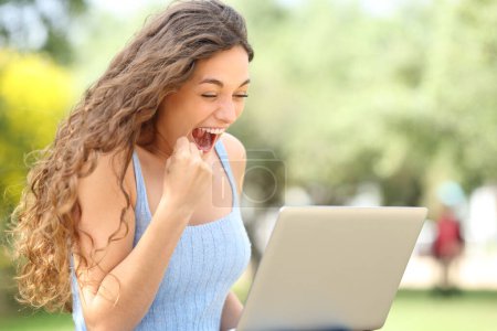 Téléchargez les photos : Femme excitée célébrant le succès avec un ordinateur portable dans un parc - en image libre de droit