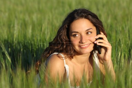 Téléchargez les photos : Femme heureuse parlant sur un téléphone portable dans un champ de blé vert - en image libre de droit
