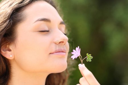 Foto de Mujer feliz oliendo flor en un parque - Imagen libre de derechos