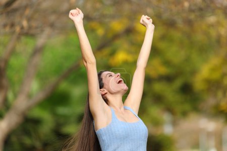 Foto de Excited teen raising arms celebrating success in a park - Imagen libre de derechos